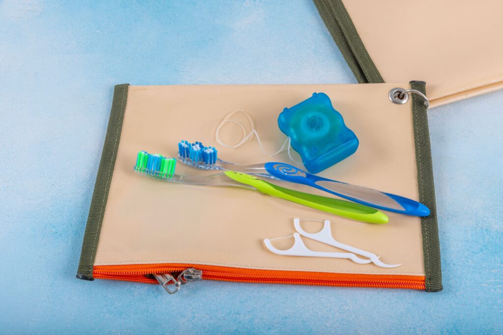 Toothbrushes, floss, and flossers on a tan, orange, and green travel pouch